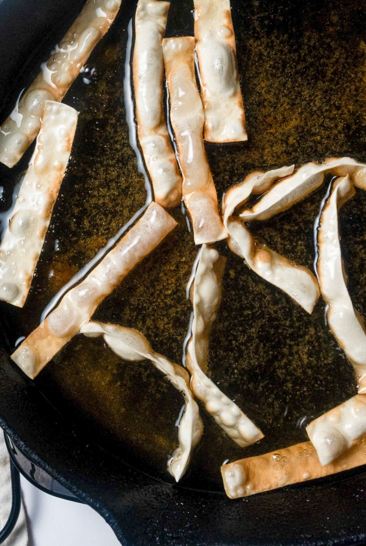 wonton strips being fried in a cast iron skillet